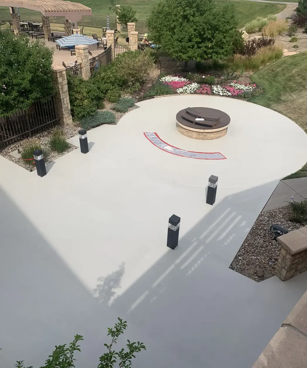 Tan coated concrete patio around a round fire pit, with lawn and landscaping beyond