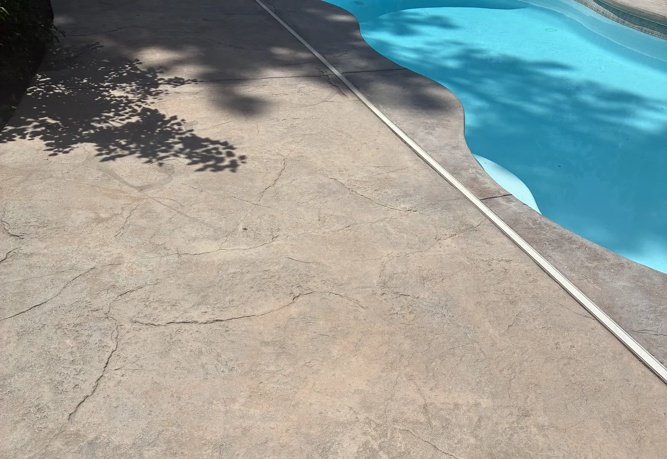 The same pool deck before the work, faded tan textured concrete with cracks