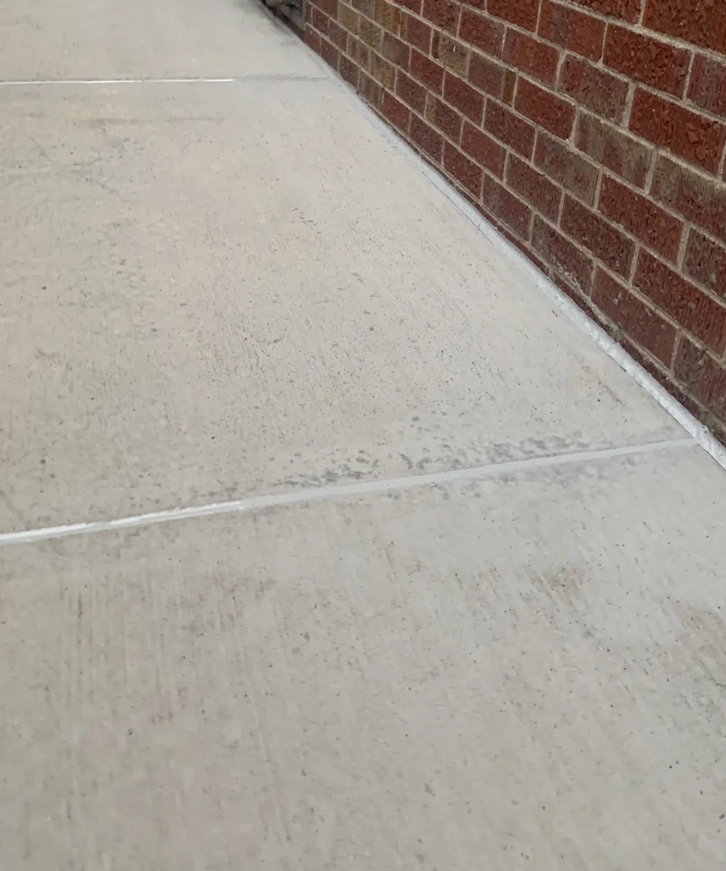 Concrete walkway with sealed joints along a red brick wall