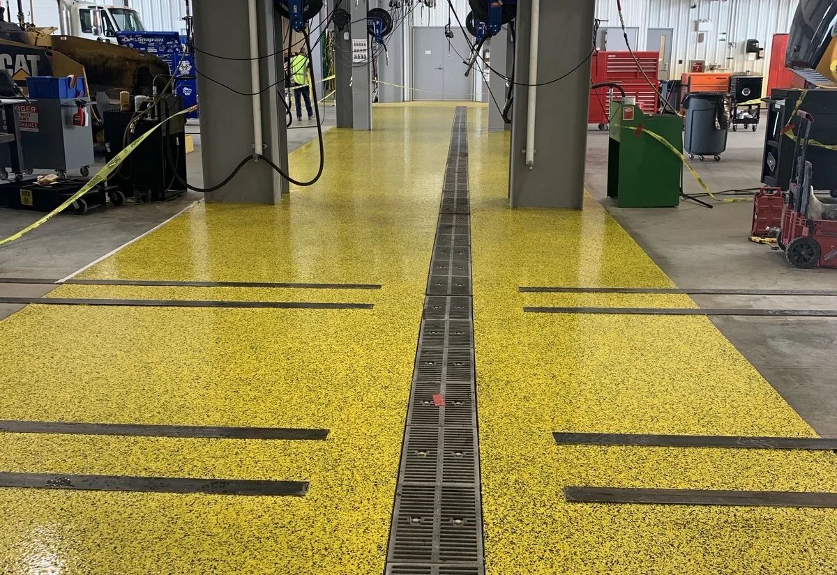Yellow flake epoxy shop floor with a trench drain between vehicle lifts